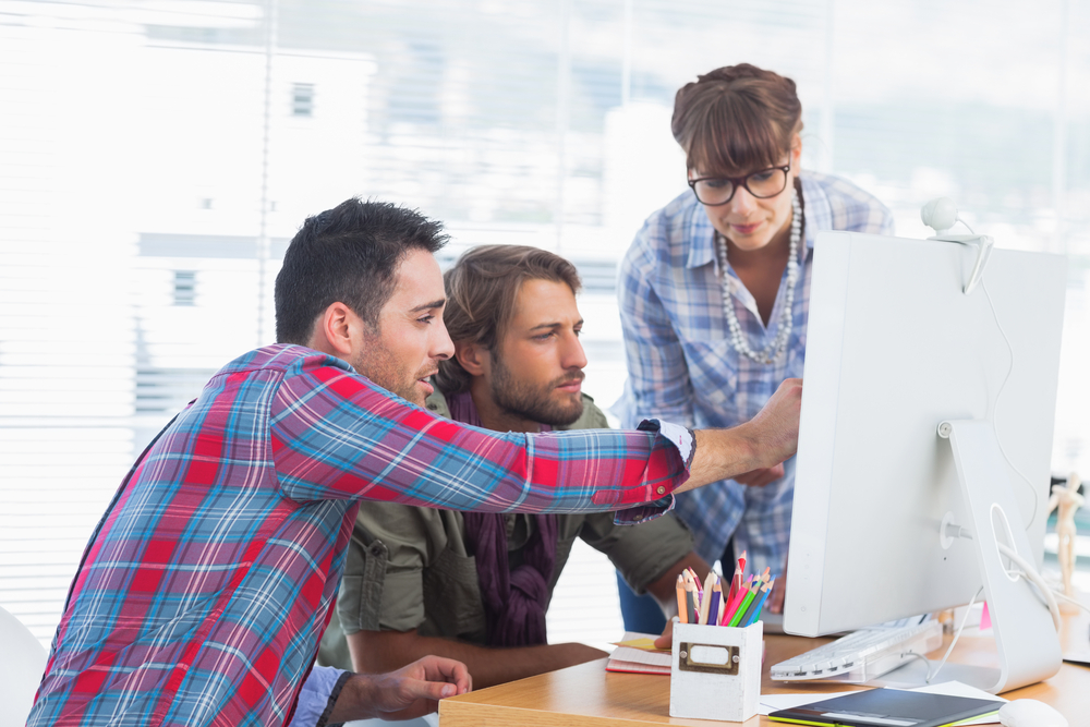 Equipo de diseñadores trabajando juntos en un ordenador Equipo de diseñadores trabajando juntos en un ordenador